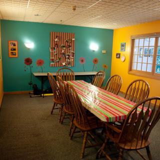A cozy dining room with vibrant teal and yellow walls, featuring a long table with a striped tablecloth surrounded by wooden chairs.