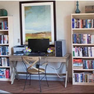 A cozy home office setup with a computer desk surrounded by bookshelves and a large painting on the wall.