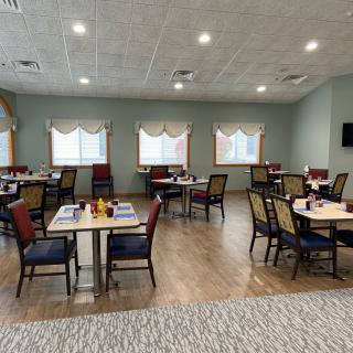 A cozy dining room with neatly arranged tables and chairs, featuring soft lighting and simple decor.