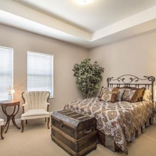A cozy bedroom with vintage decor, featuring an elegant armchair and a classic trunk at the foot of the bed.