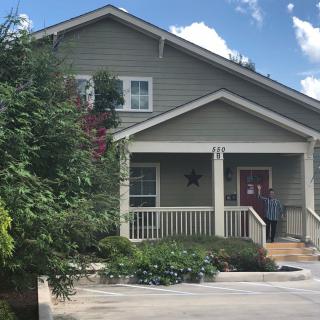 A charming house with a front porch and surrounding garden greenery under a cloudy blue sky.