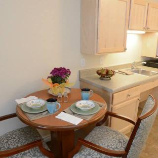 A cozy kitchenette with a small dining setup featuring two chairs, plates, and flowers.