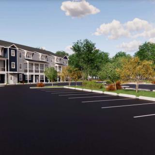 A modern apartment complex with a spacious parking lot and surrounding greenery under a cloudy sky.