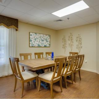 A well-lit dining or meeting room featuring a large wooden table surrounded by chairs, with artwork adorning the walls.