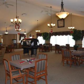 A spacious dining hall with neatly arranged tables and chairs, decorated with chandeliers and large windows.