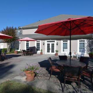 A spacious patio with red umbrellas and outdoor seating in front of a large house on a sunny day.