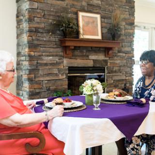 Two women enjoying a meal together at a beautifully set table, with a cozy stone fireplace in the background.