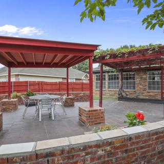 A cozy patio with a pergola and outdoor seating next to a brick house.
