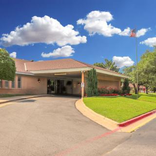 A building with a covered driveway surrounded by greenery under a blue sky with clouds.