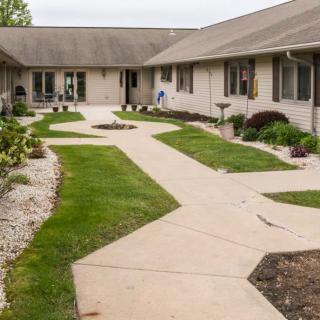 A landscaped courtyard with a paved walkway surrounded by grass and a single-story building.
