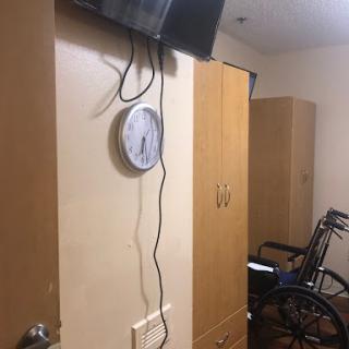 A cozy room featuring a wardrobe, a wall clock, a TV, and a wheelchair.