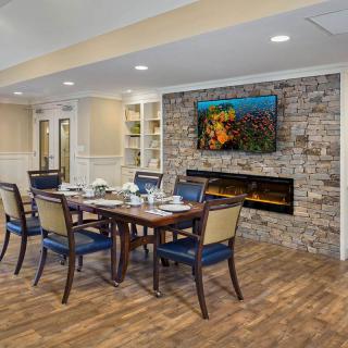 A cozy dining room with a wooden table and chairs, featuring a stone fireplace and a mounted television.