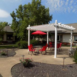 A sunny garden patio with a white pergola, red chairs, and an umbrella.