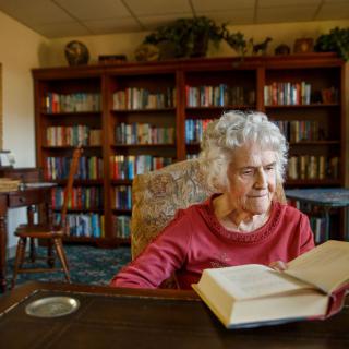 An elderly woman reading a book in a cozy library setting.