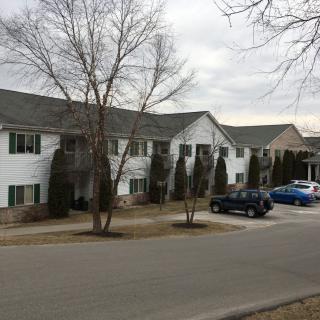 A residential apartment building with parked cars and bare trees on an overcast day.