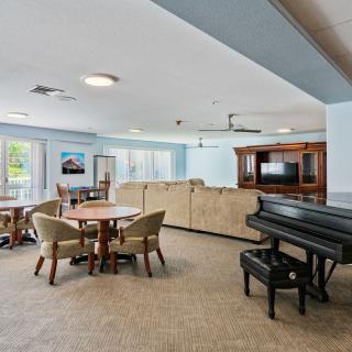 A spacious living room featuring a piano, comfortable seating, and a TV entertainment center.