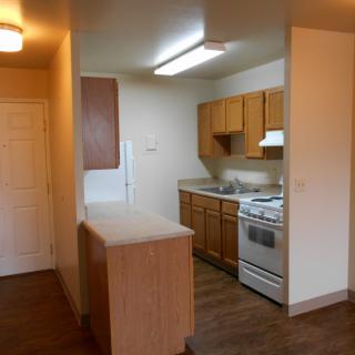 A compact apartment kitchen with wooden cabinets and a gas stove.