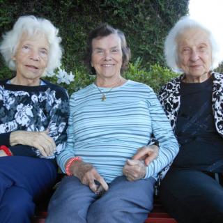 Three elderly women sitting together outdoors, smiling.