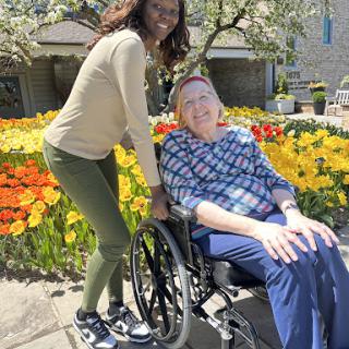 A joyful moment shared between a caregiver and an elderly person in a vibrant garden.