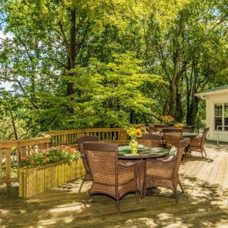 A sunny outdoor deck with wicker patio furniture surrounded by lush trees.
