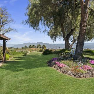 A beautifully landscaped garden with lush green grass, colorful flower beds, and tall trees under a clear blue sky.