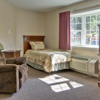 A cozy bedroom with a single bed, an armchair, and a large window letting in natural light.