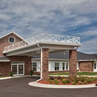 A brick building with a covered entrance and landscaped surroundings under a partly cloudy sky.