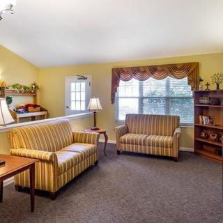 A cozy living room with striped couches, a bookshelf, and large windows.
