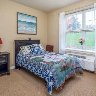 A cozy bedroom with a single bed, colorful bedding, and a large window bringing in natural light.