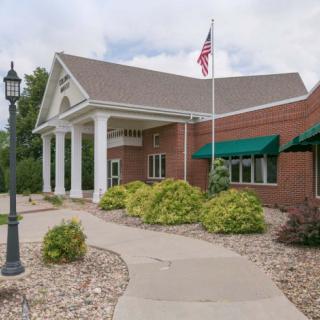 A brick building with white columns, green awnings, and an American flag.