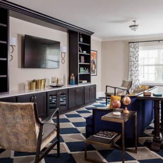 A modern living room featuring a large television, built-in shelves, and stylish armchairs with a geometric rug.