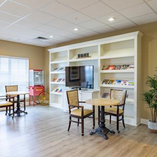 A cozy seating area with tables, chairs, and a large television set in front of built-in shelves.