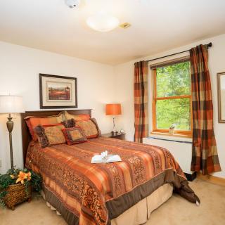 A cozy bedroom with warm-toned bedding and matching curtains, featuring a window view and soft lighting.