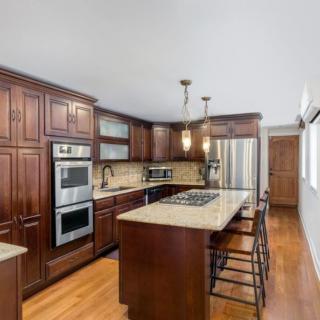 A modern kitchen featuring wooden cabinets, a central island with bar stools, stainless steel appliances, and pendant lighting.