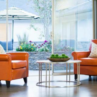 A modern living room with bright orange chairs and a sleek glass table in front of large windows.