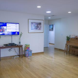 A modern living room with wooden floors, featuring a TV and a piano.