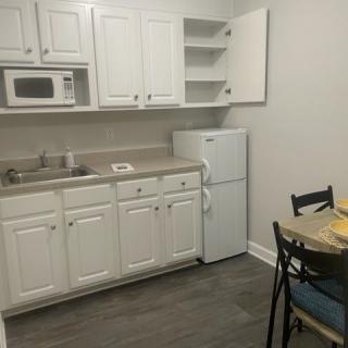 A small kitchen area with white cabinets, a microwave, refrigerator, and a dining table with chairs.