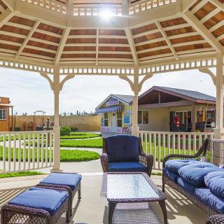 A cozy outdoor gazebo with comfortable seating, overlooking a sunny garden.