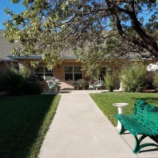 A serene garden view with a pathway leading to a house, flanked by trees and a green bench.