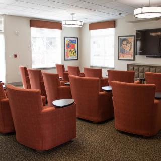 A comfortable seating area with red chairs arranged in rows, featuring a television and large windows for natural light.
