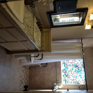 A well-lit bathroom with a sink, mirror, toilet, and a shower area featuring a stained glass window.