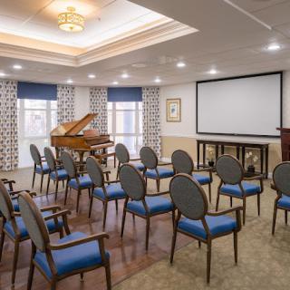 A modern conference room featuring a setup with chairs, a grand piano, and a projector screen.