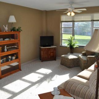 A cozy living room with a sofa, television, bookshelves, and ample natural light coming through the windows.