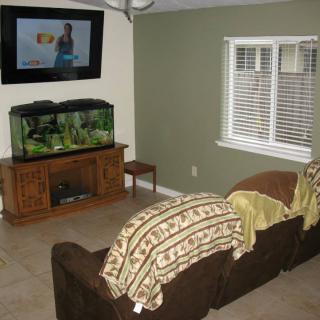 A cozy living room with a sofa, a fish tank, and a mounted TV, featuring blankets draped over the furniture.