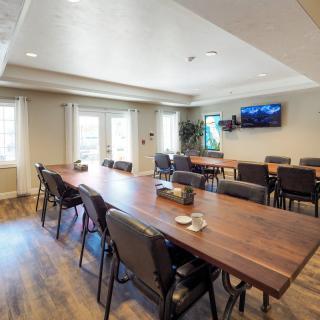 A modern conference room with a large wooden table, several chairs, and a television on the wall.