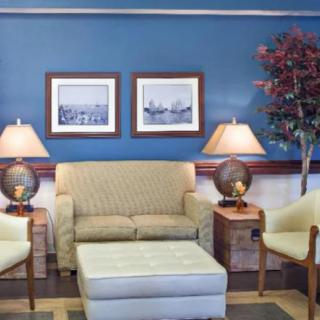 A cozy living room with a sofa, two chairs, and lamps on side tables, framed by artwork on the wall.