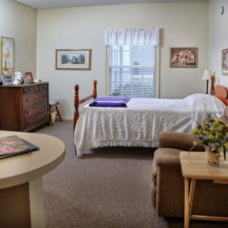 A cozy bedroom with a neatly made bed, dresser, and armchair.
