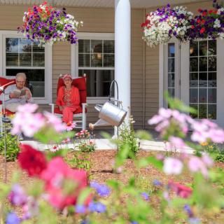 A colorful garden view with flowers and people relaxing on a porch.