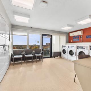 A modern laundry room featuring washing machines, dryers, and a comfortable waiting area with large windows.
