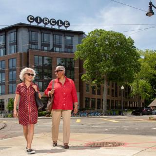 A couple strolling in an urban area with a modern building and trees in the background.